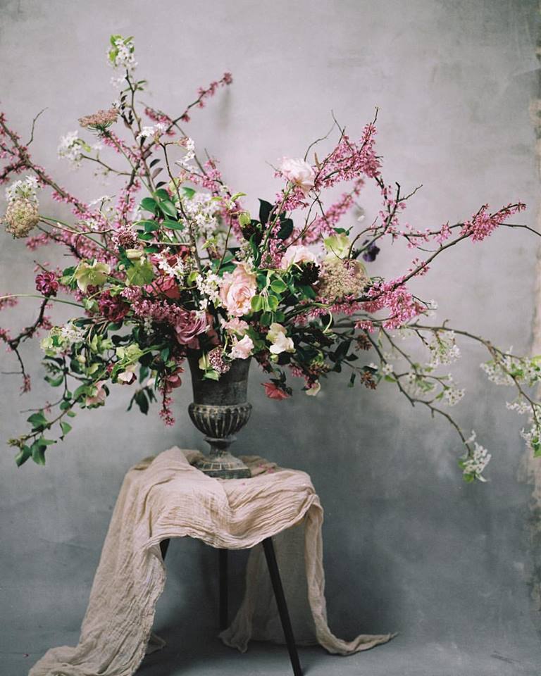 A large floral arrangement in an antique vase with long pink branches by Maxine Owens