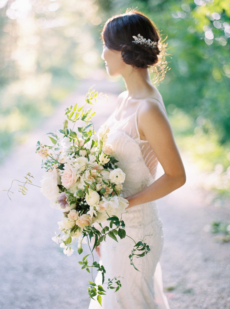 A bride in her dress holds a bridal bouquet by Heather Siu