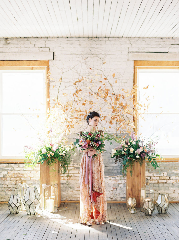 A model holds a bouquet and stands between 2 stands with floral arrangements by Eatherley Schultz