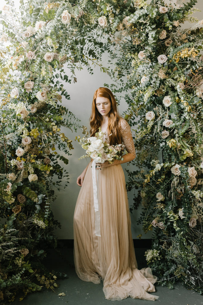 A model poses in a bridal gown under a floral arch made at the Mayesh Design Star Workshop