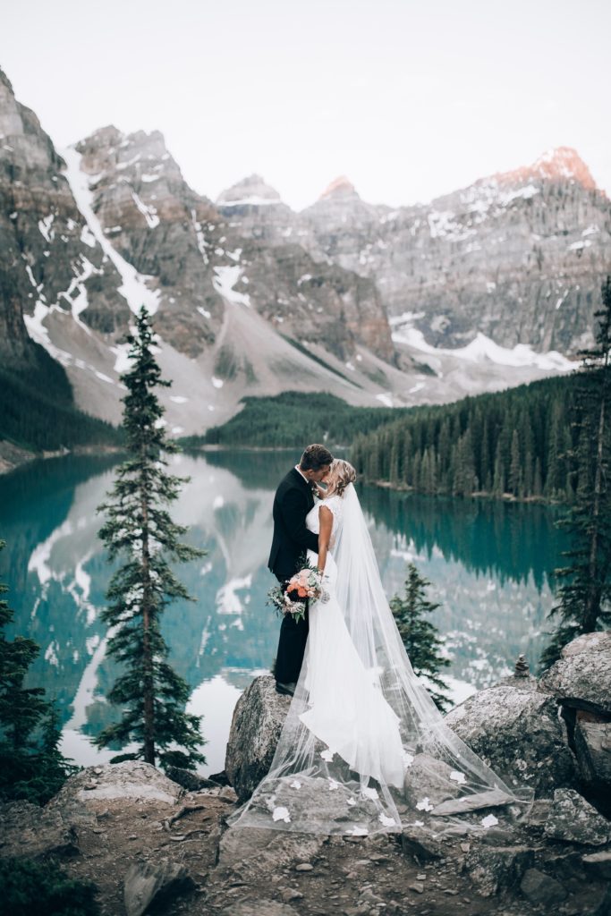 A bride and groom kiss at flowers in the Rockies at Moraine Lake