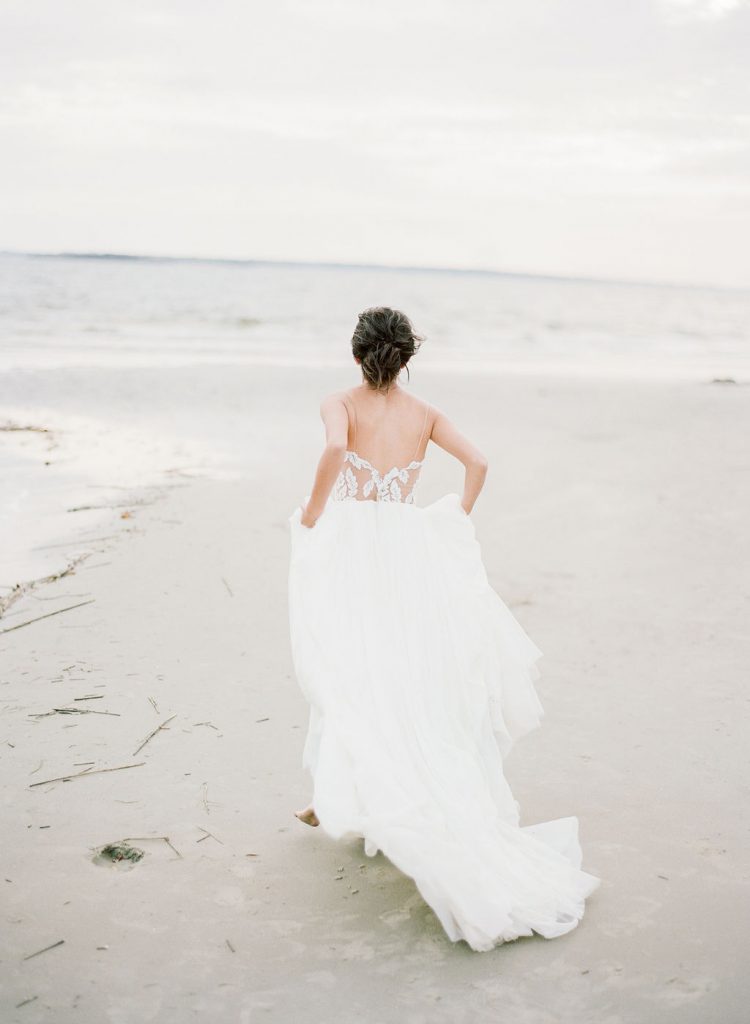A bridal photo shoot model walking toward the ocean on the beach in a wedding dress