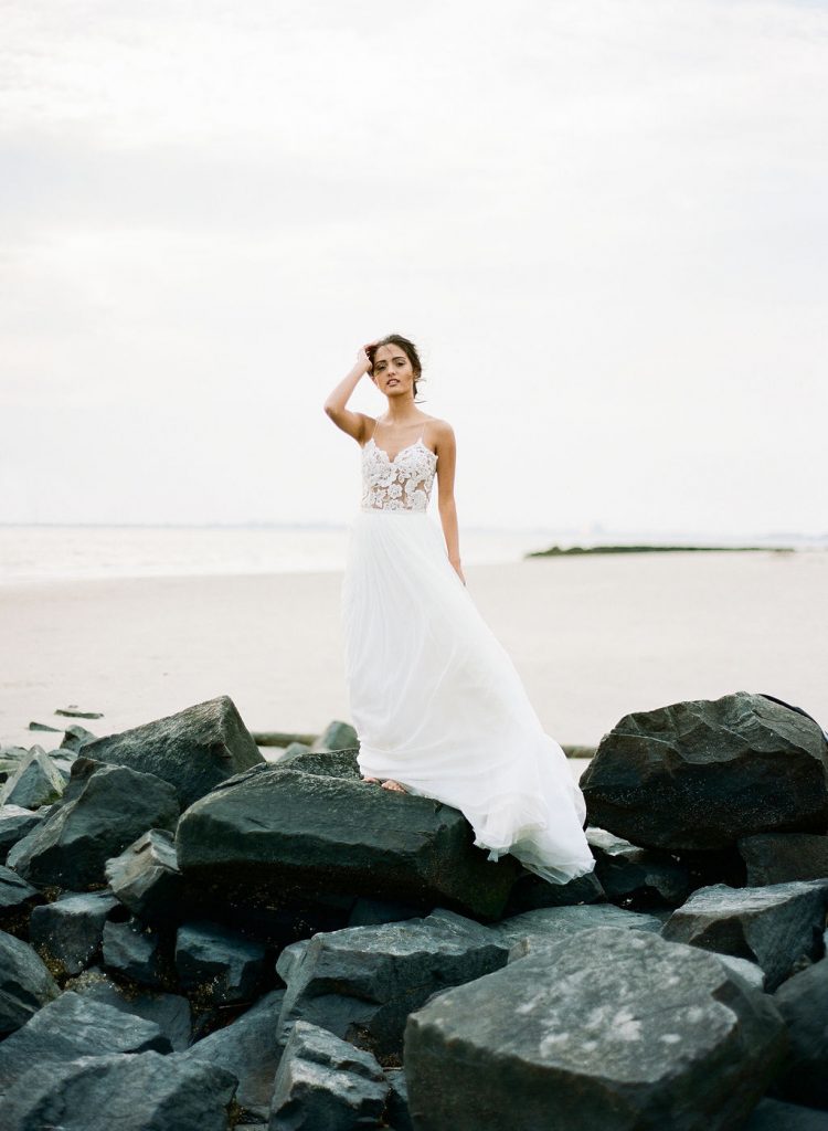 A model for a bridal photo shoot standing on rocks on the beach