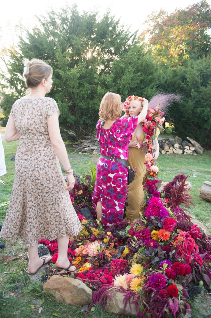 Parie Donaldson wears a floral headdress and stands in a large, red floral arrangement