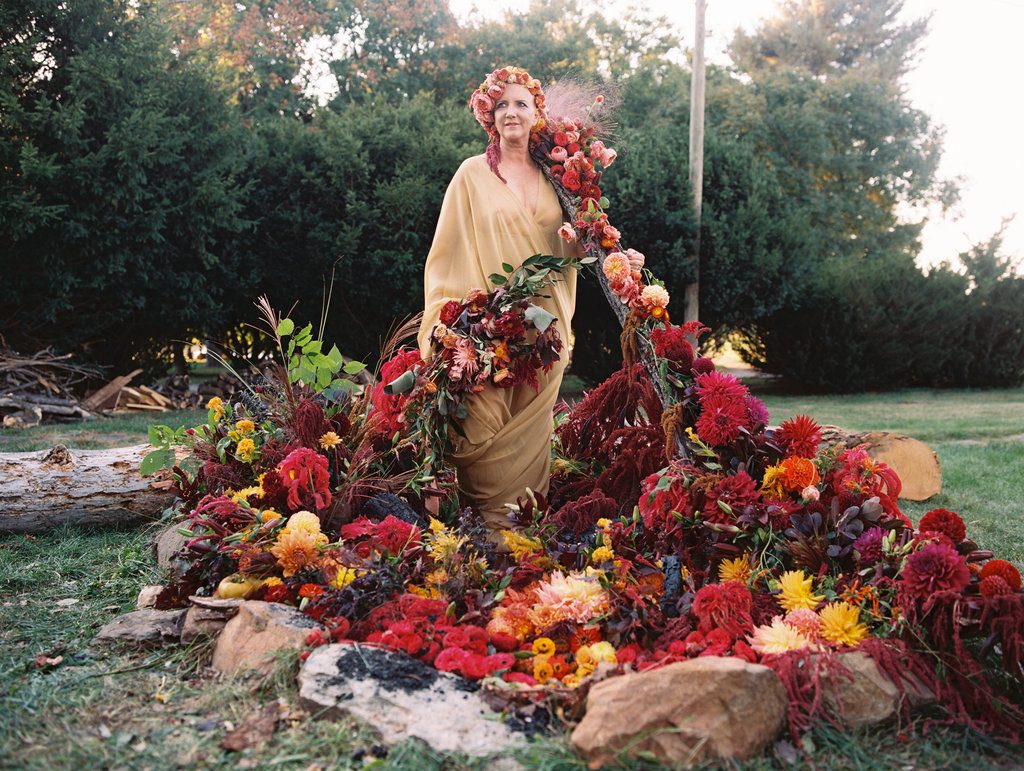 Parie Donaldson wears a floral headdress and stands in a large, red floral arrangement