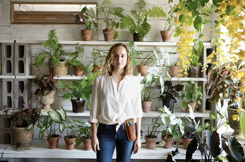 Liza Lubell stands in front of a wall of potted green plants
