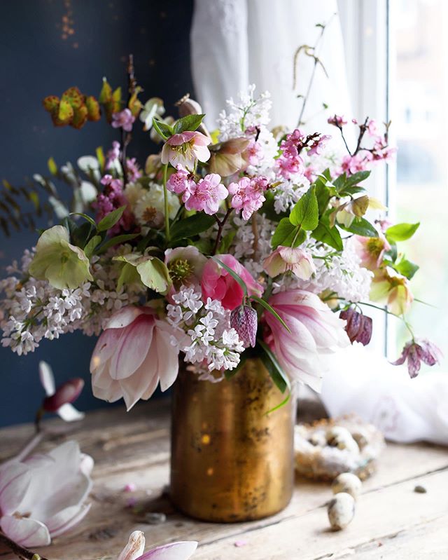 A pink floral arrangement sits in a golden vase by Janne Ford