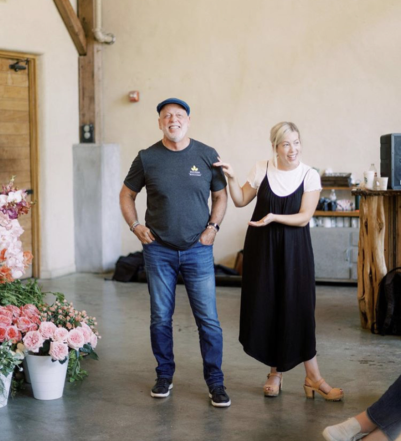Ali Dahlson and her father, Pat, stand in a floral studio with a concrete floor and wooden-accented walls