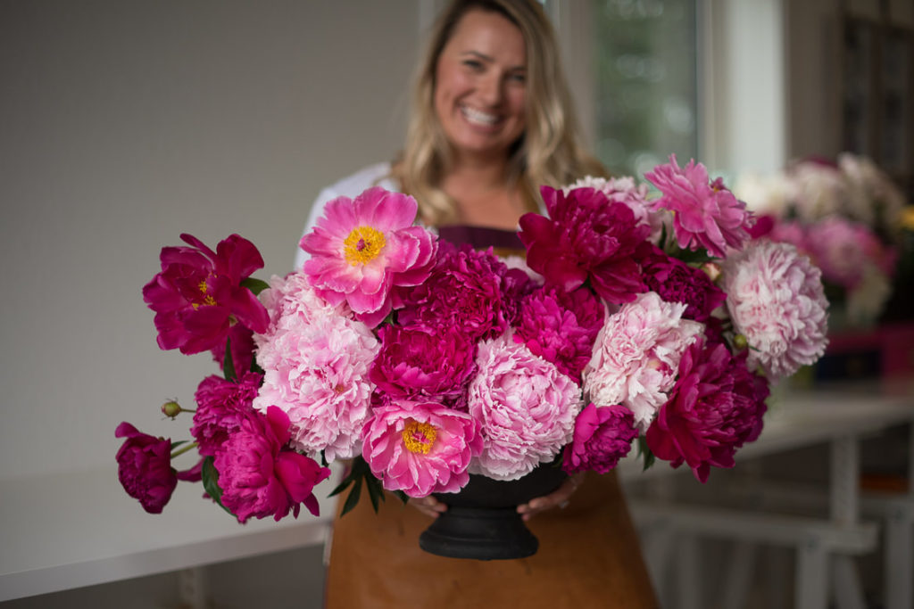 BB Podcast guest, Rachelle Willows, holds a bright pink floral arrangement in a black vase