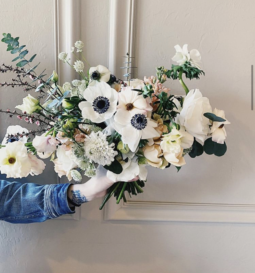 A wedding florist holds a white bridal bouquet from outside the frame