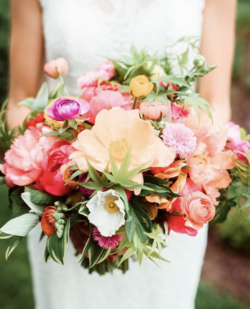 A bride holding a bouquet of pink and coral flowers made by Ellen Frost, owner of Local Color Flowers