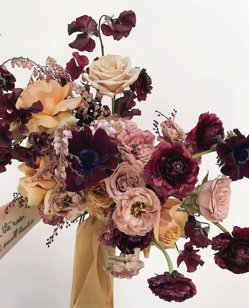 bridal bouquet of lisianthus, sweet peas, roses, and ranunculus in shades of mauve, burgundy and butterscotch