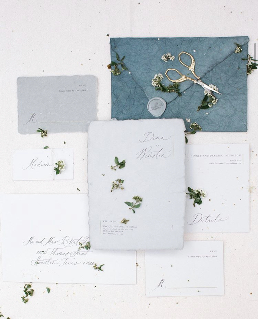 Handmade paper wedding inviation suite, tiny blooms, and gold handled snips as part of a professional flatlay