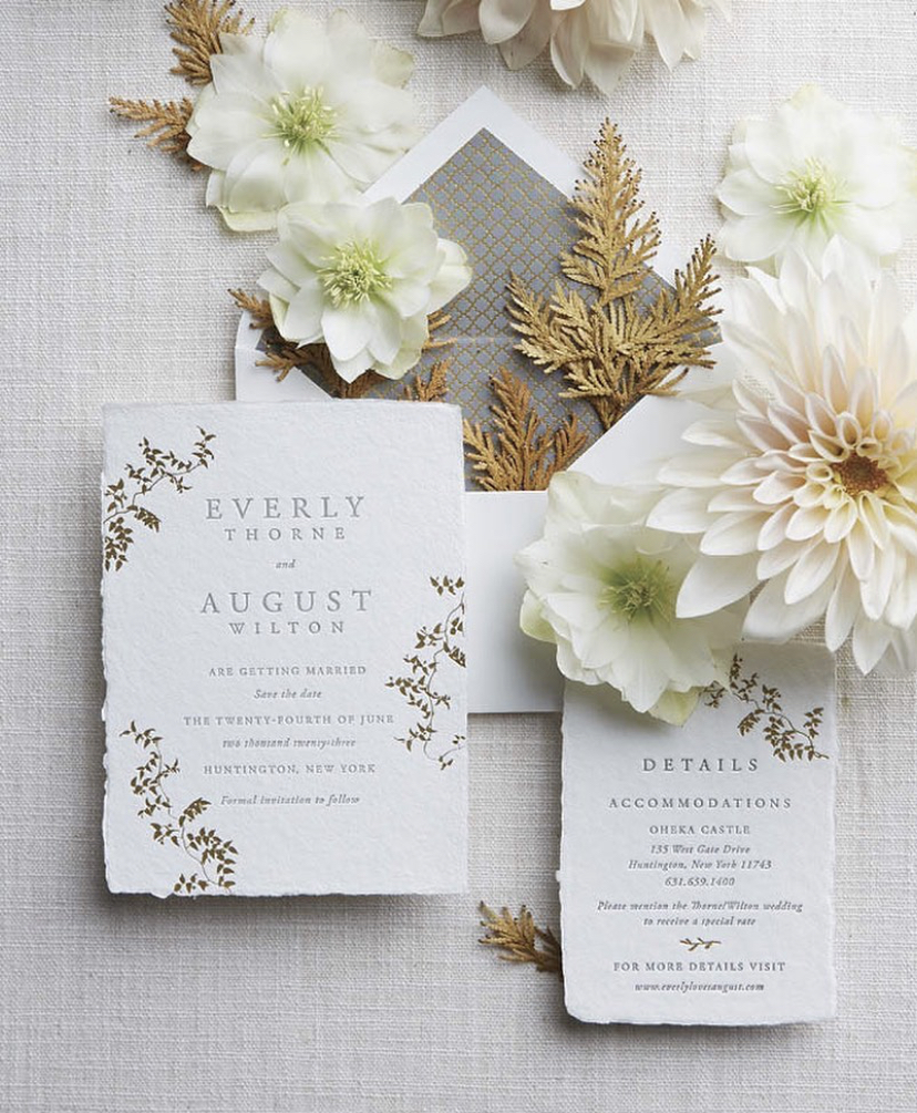 Cream flowers and bronze foliage decorate a wedding invitation flatlay