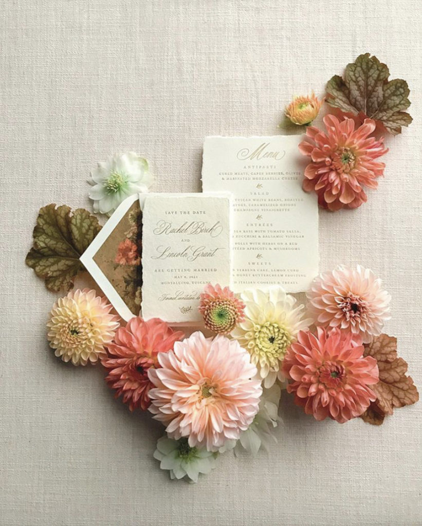 Flatlay of peach flowers, brown foliage, and matching wedding invitation 