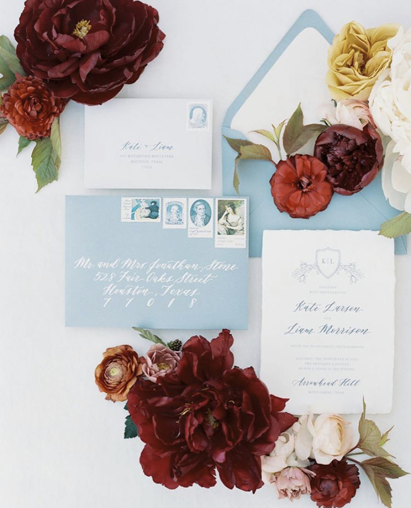 A flatlay of deep red blooms and sky blue invitation set