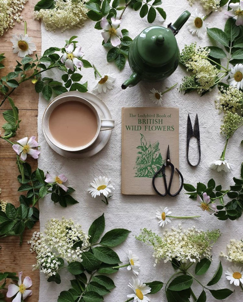 Flatlay of green and white flowers, a cup of coffee, green teapot and garden snips