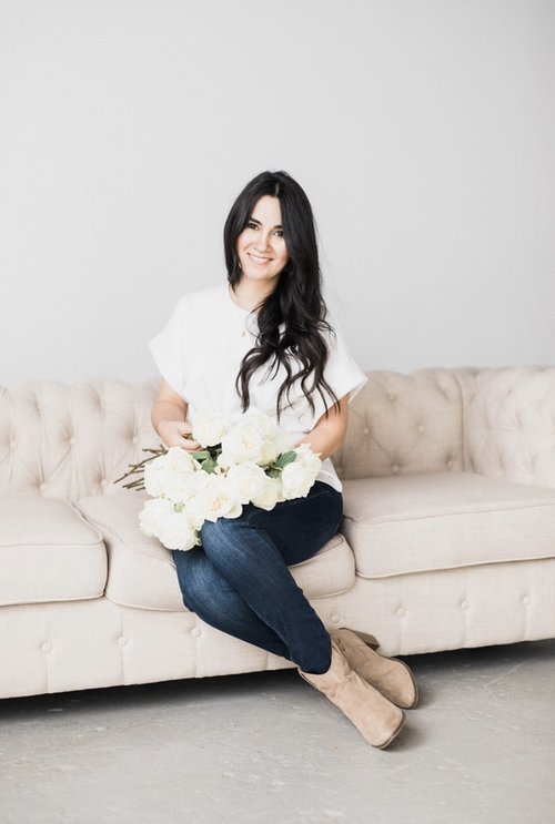 Wedding and Event Florist Maria Maxit of Maxit Flower Design sitting on a cream colored sofa holding a handful of white roses while sharing tips on floral business profitability
