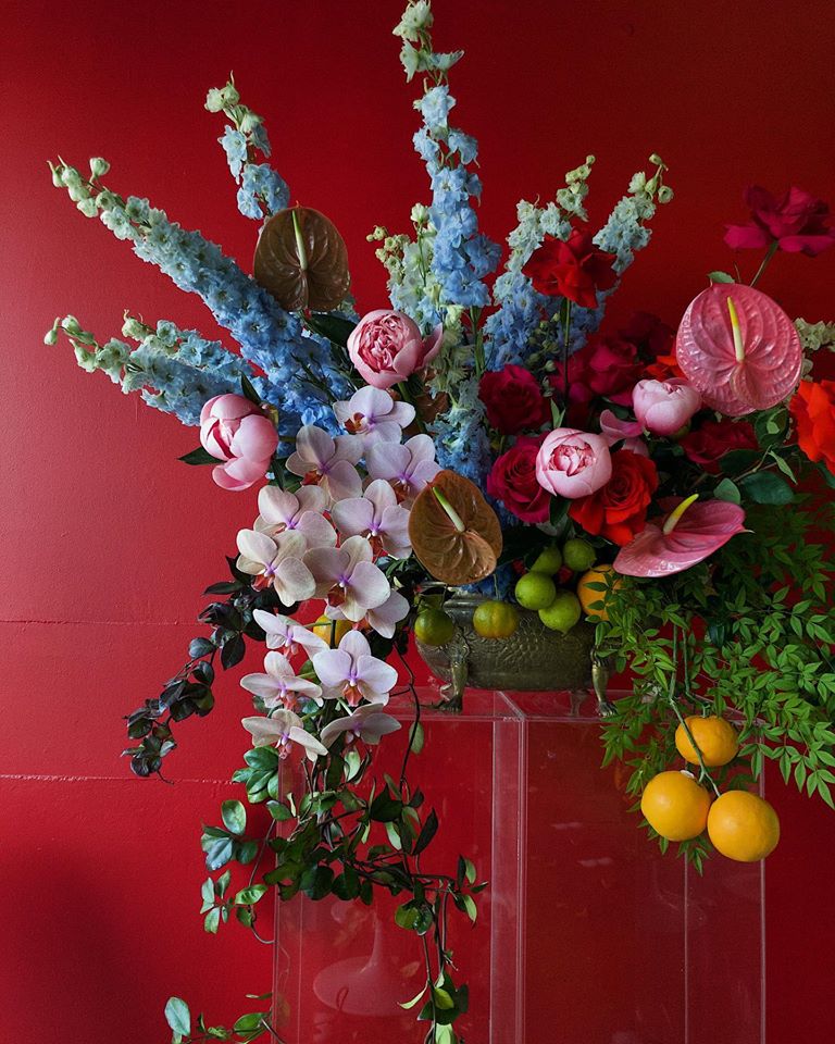 A large floral arrangement in blue, pink, and red with lemons and limes by Rebecca Grace