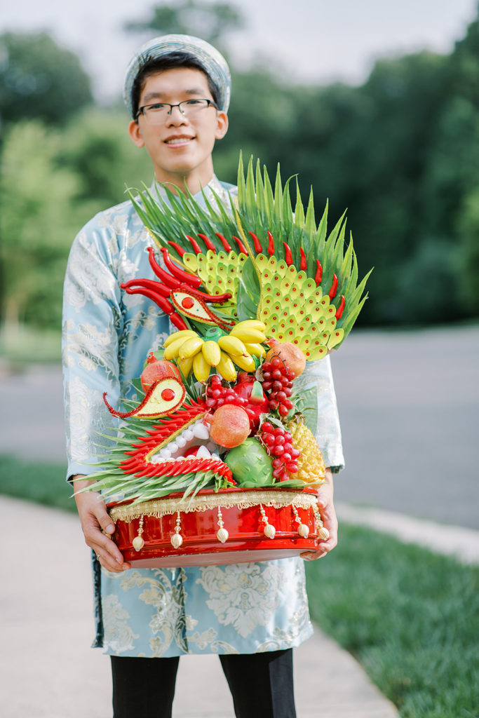 young man carry a gift platter during the processional as part of the Vietnamese wedding tradition