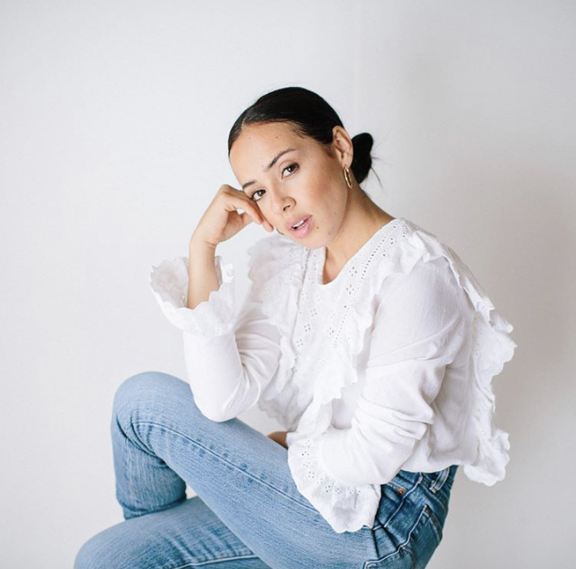 Florist Lily Roden in jeans and a white shirt sitting on a stool