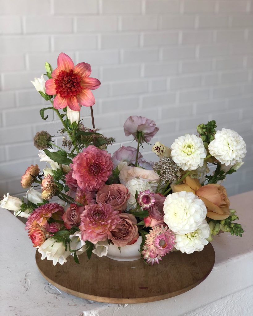 Floral arrangement of dahlias, sweet peas, roses and strawflowers designed in a bowl by The Wild Mother sitting on a wooden lazy susan