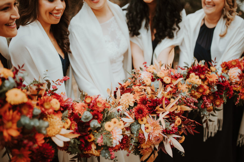 bride and her bridesmaids holding autumn bouquets of local flowers in shades of rust and peach