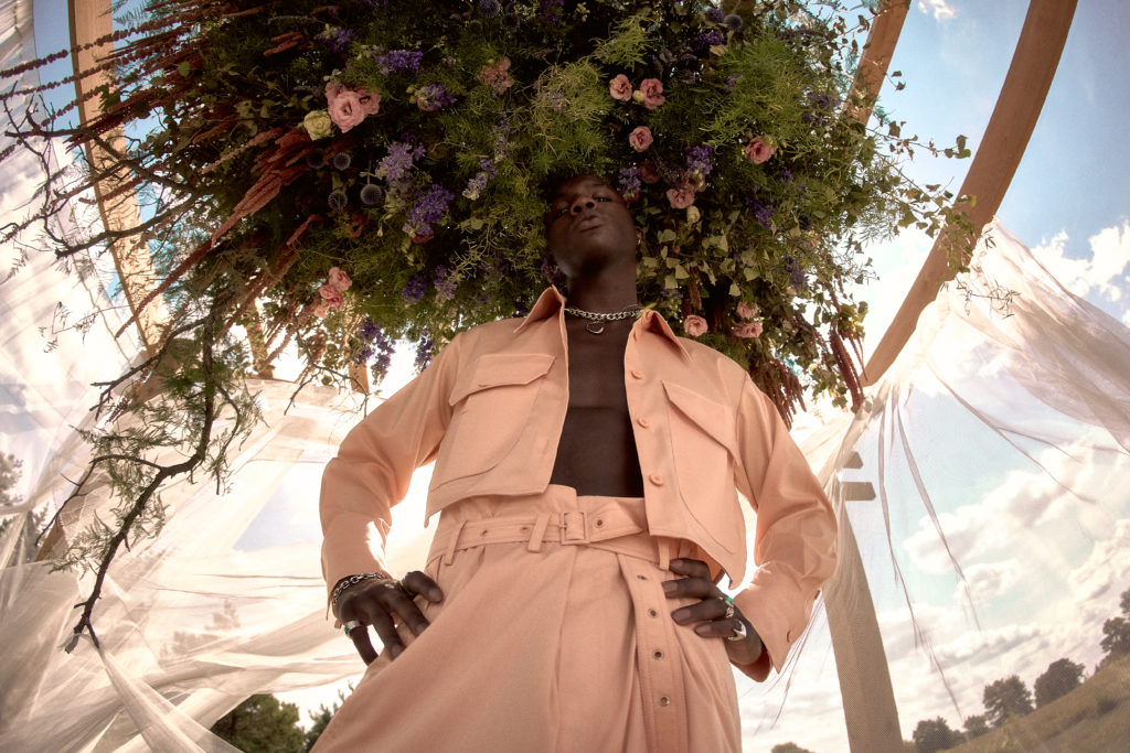  high fashion photo shoot of a man standing beneath a floral chandelier