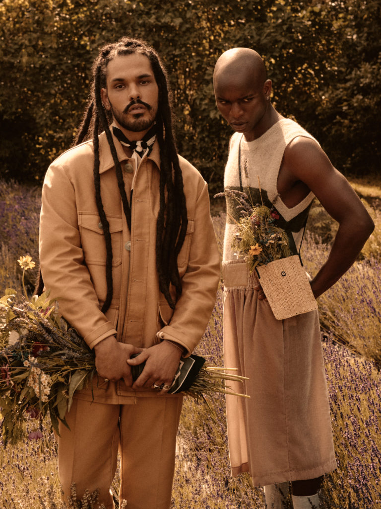 two men holding flowers in a field for a high fashion photo shoot