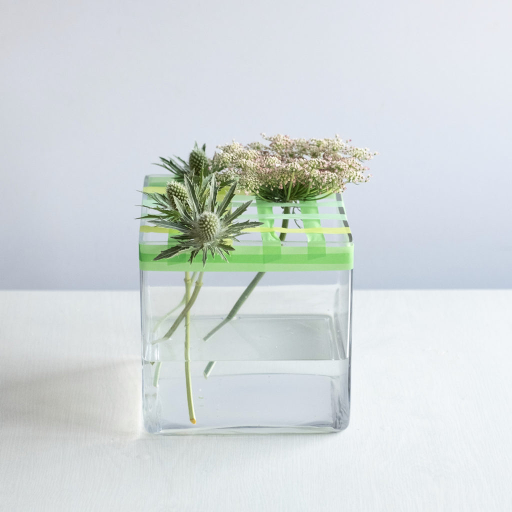 thistle and ammi rest against a washi tape grid on a glass vase in a floral tutorial