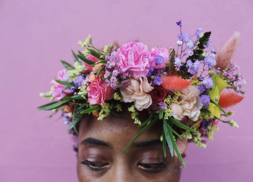 Woman wearing a colorful Brooklyn Blooms flower crown in front of a pink wall