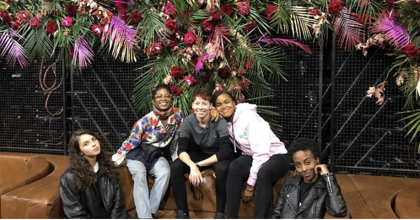 The Brooklyn Blooms team sitting in front of a flower wall they created