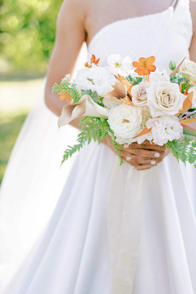 Bride in white wedding gown holding a Floraison Paris bouquet of orange cosmos, fern, and ivory roses and callas