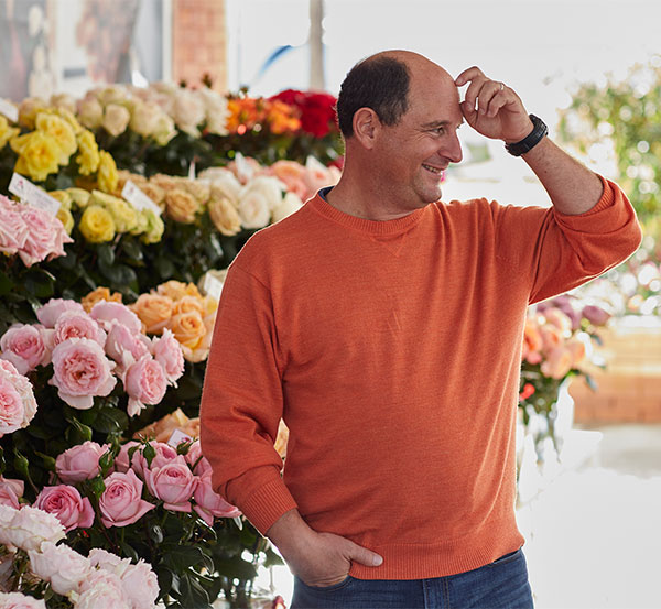 Alexandra Farms owner Joey Azout in orange sweater standing in front of a wall of buckets filled with colorful garden roses