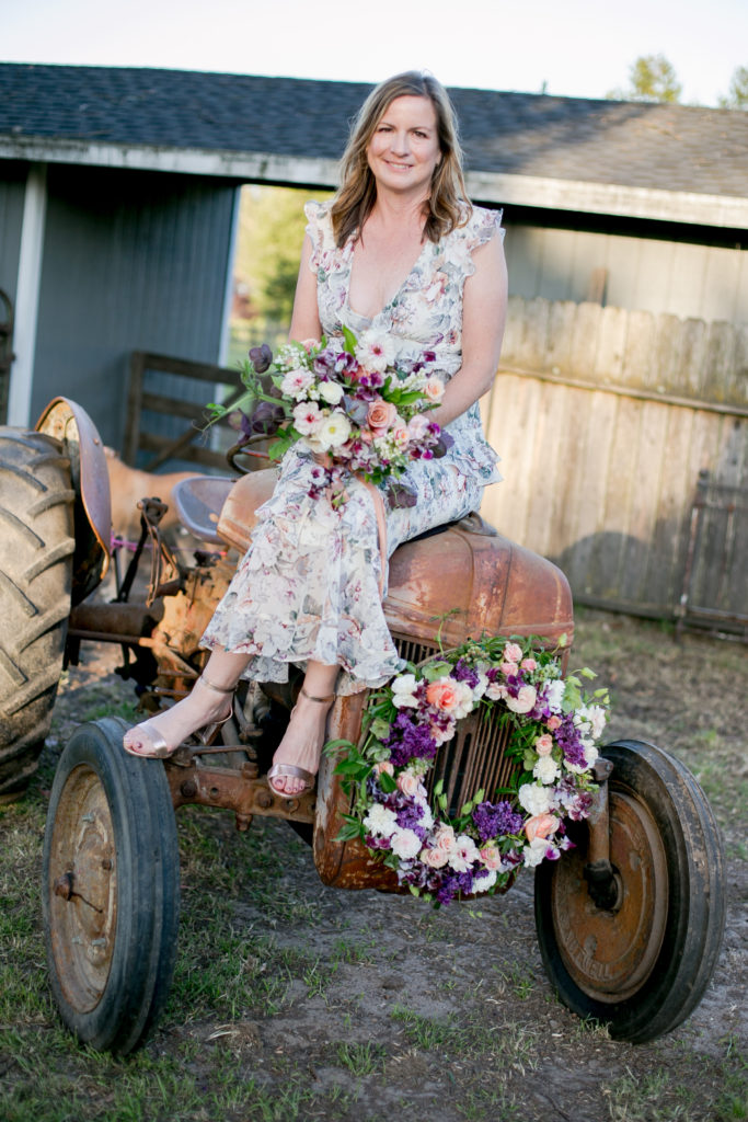 Susan sitting on antique tractor on her wedding day in a floral dress holding a bridal bouquet designed by Marion Moss Floral Design