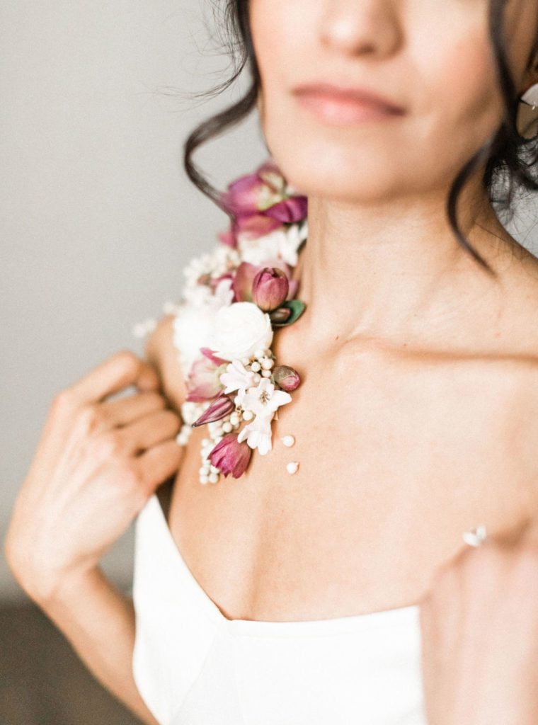 Woman in white off the shoulder dress and wearable florals on shoulder in white and mauve