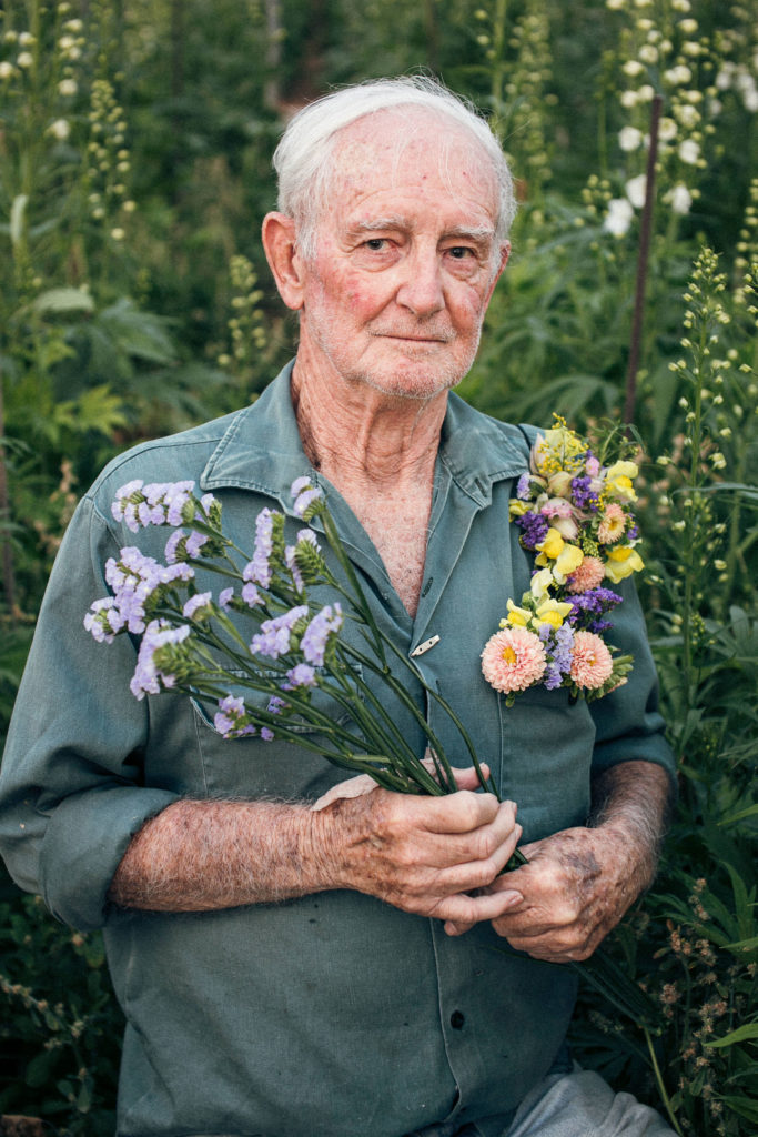81 year old flowered fella holding a bunch of limonium while wearing a floral pocket square and surrounded by cut flowers