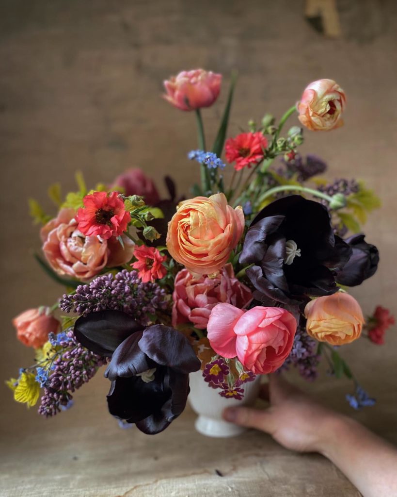 Floral arrangement by Florist Anna Potter of Swallows and Damsons with peach ranunclulus, lilac, and black tulips in a white footed bowl