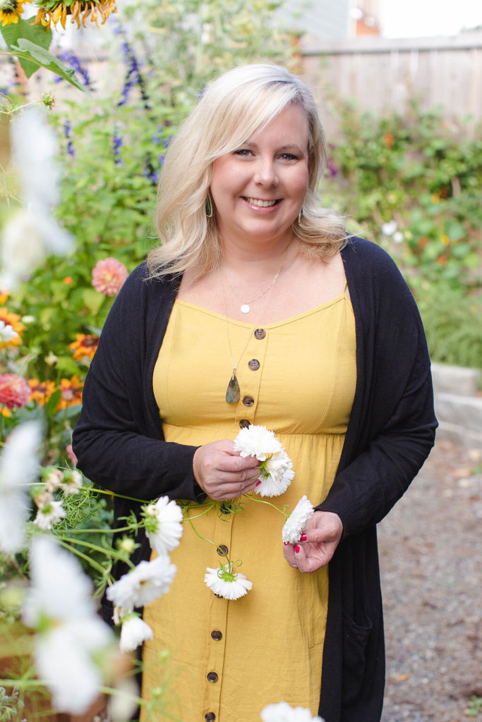 Kelly Shore, owner of The Floral Source, wearing a yellow dress and black sweater and standing in a cutting garden