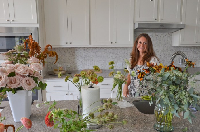 the founder of EveryStem floral ordering app standing in her kitchen surrounded by buckets and vases of flowers