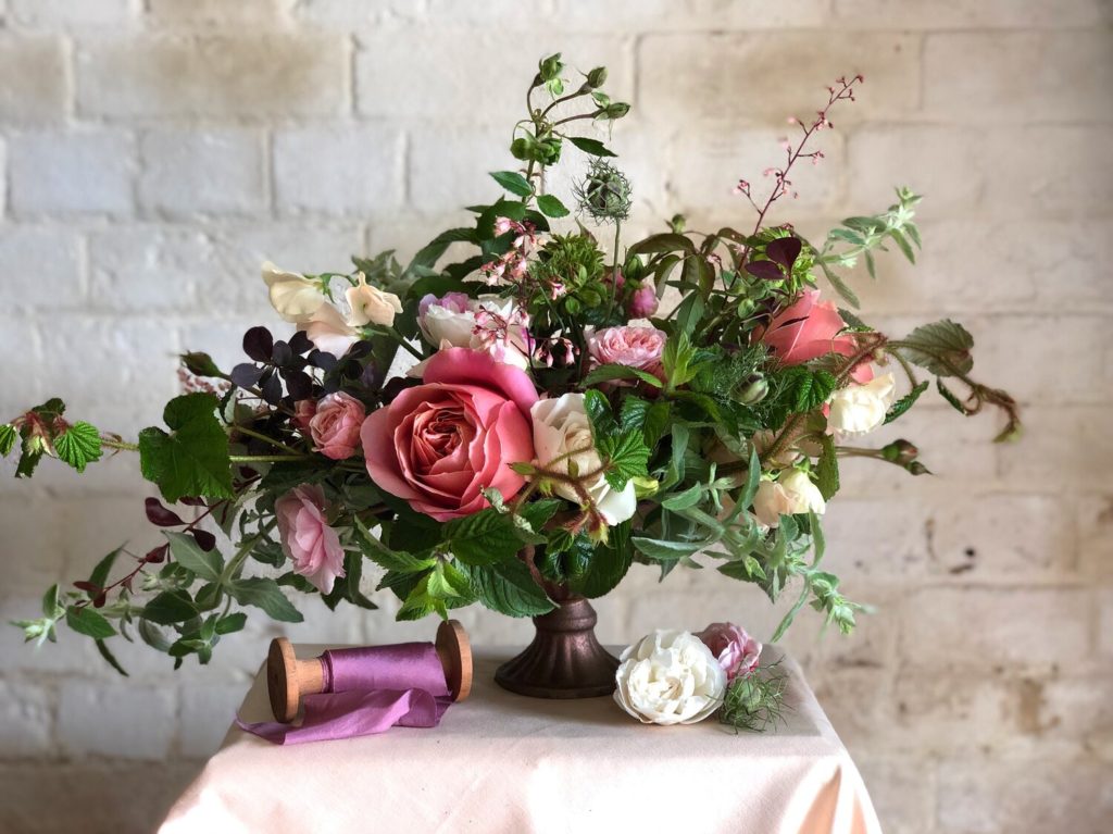 Floral arrangement of roses and greenery in a footed vase designed by floral designer Sarah Diligent