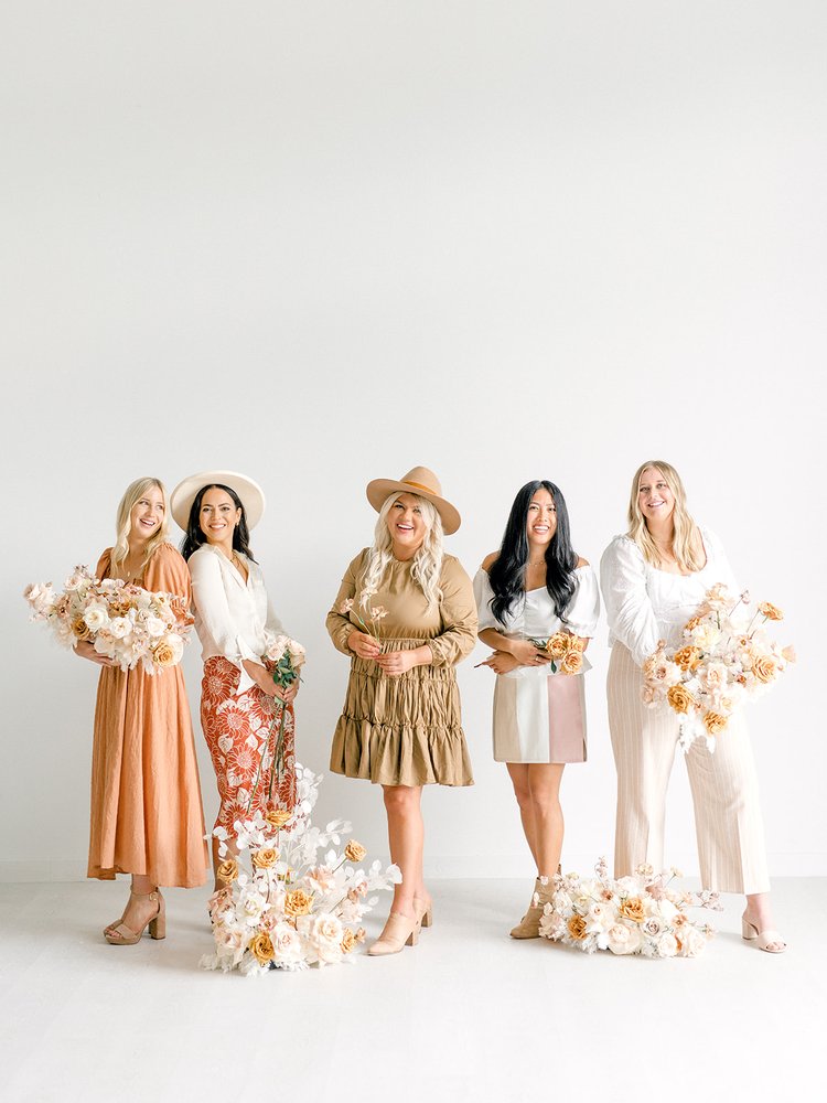 Five women on the Remi + Gold Floral Design team of destination weddings florists in neutral toned clothes and holding neutral floral arrangements 