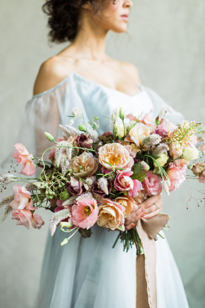 Bride in a pale blue dress holding a taupe and peach bouquet designed by floral designer Ginny Early of Enemies of the Average