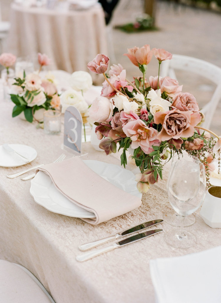 Mauve roses in centerpiece arrangements surrounded by white dishes and glass goblets of a reception table