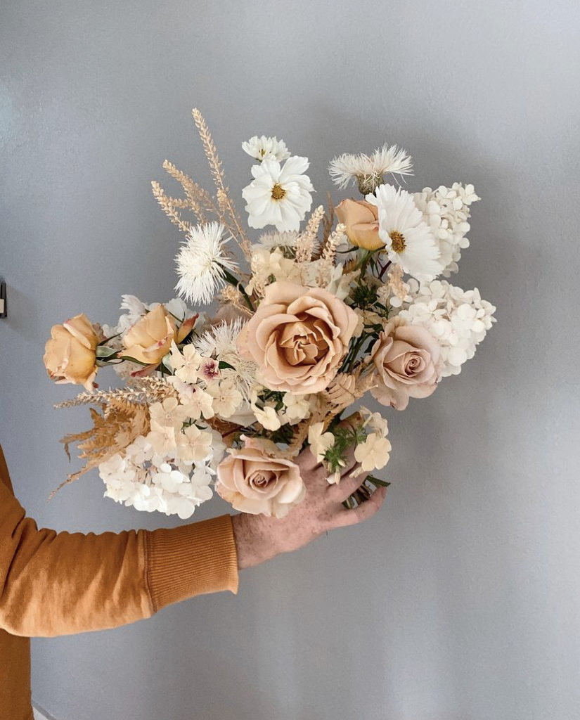 Florist Brooke Snodgrass of Seventh Stem holds a bridal bouquet of taupe and neutral tones including cosmos, phlox, roses, and hydrangea