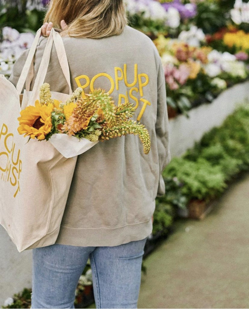 Popupflorist branded bag and sweatshirt with yellow lettering and yellow flowers in the bag
