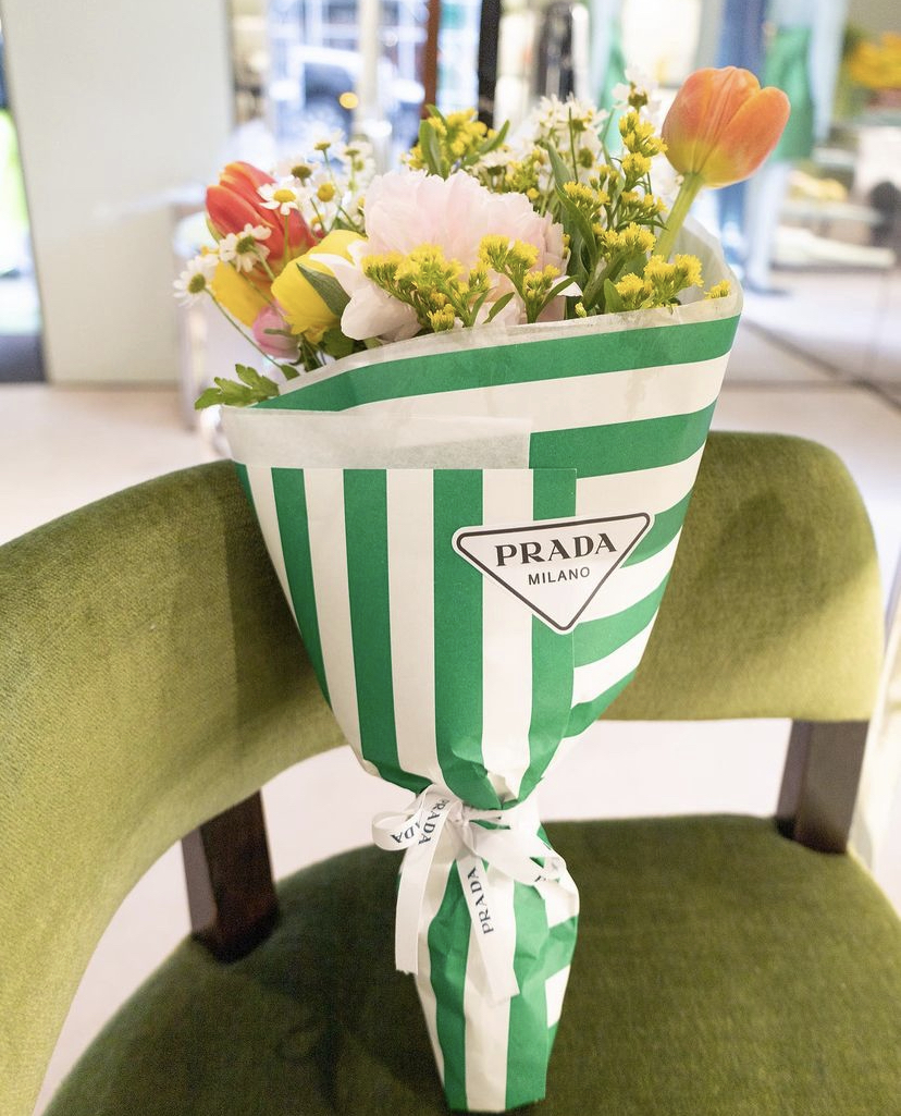 A bouquet made by Popupflorist is wrapped in green and white striped paper with Prada branding and sitting on a green velvet chair 