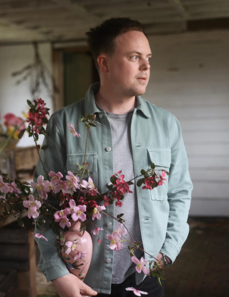Floal designer Graeme Corbett of Bloom & Burn in his studio holding a pink flower arrangement