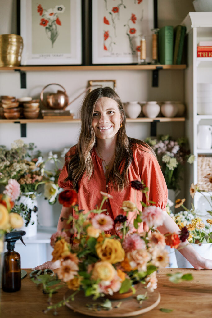 Carrington Winkelmann standing in her Austin flower studio with a centerpiece of flowers