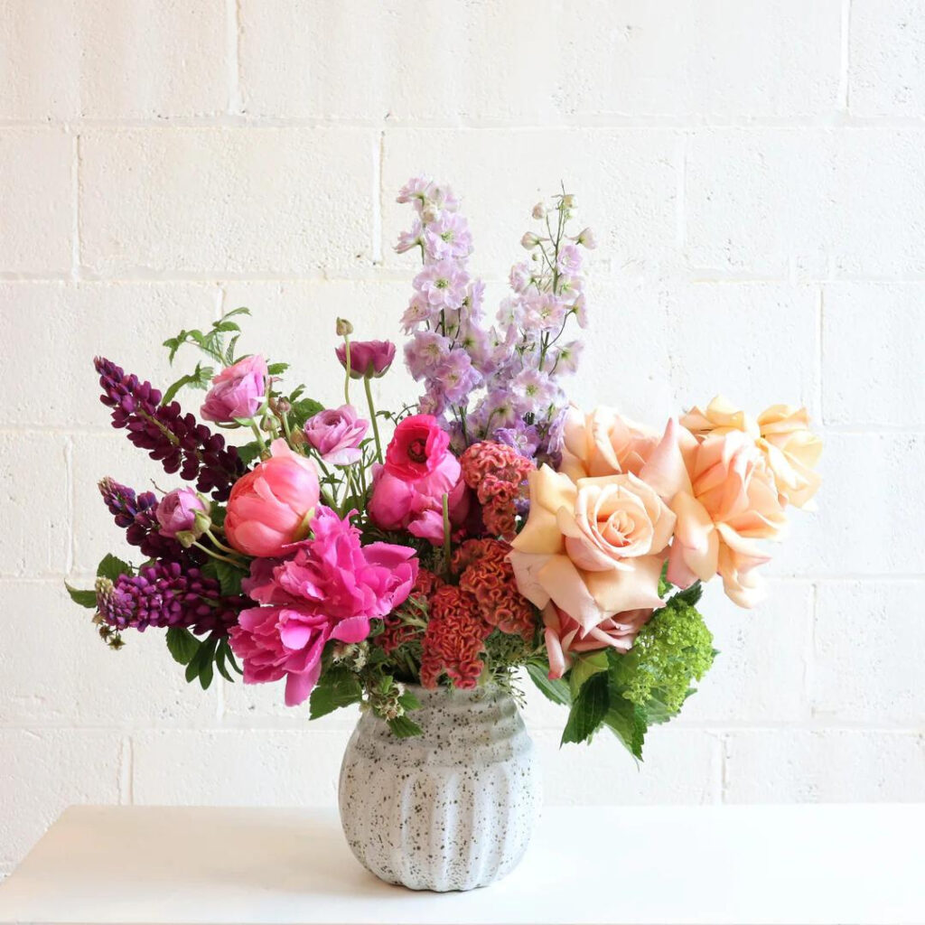 a flower arrangement of peach roses, lavender larkspur and pink peonies available in New York flower shop Stacy K Floral
